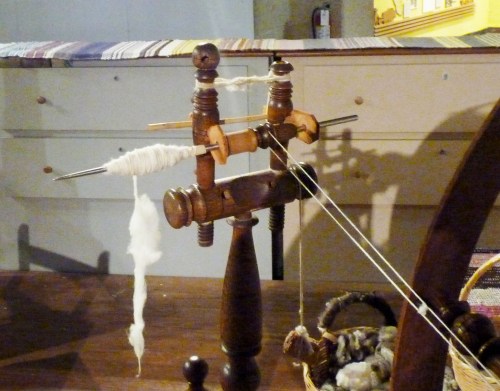 The drive band from the wheel (here it is not in the proper position) turns the metal spindle quickly. Unspun fiber is held at an angle off the tip; the twist travels up and turns the loose fiber into a thread.