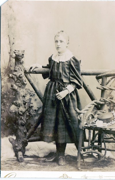 The 1880s were the heyday of the studio prop. This picture is full of them, with a fake tree stump, a fence, a rustic chair, and two animal skin rugs.